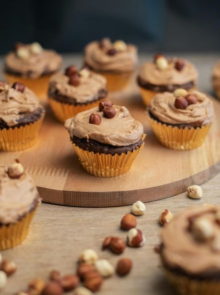 Close-up of chocolate cupcakes with hazelnut topping on a wooden board.